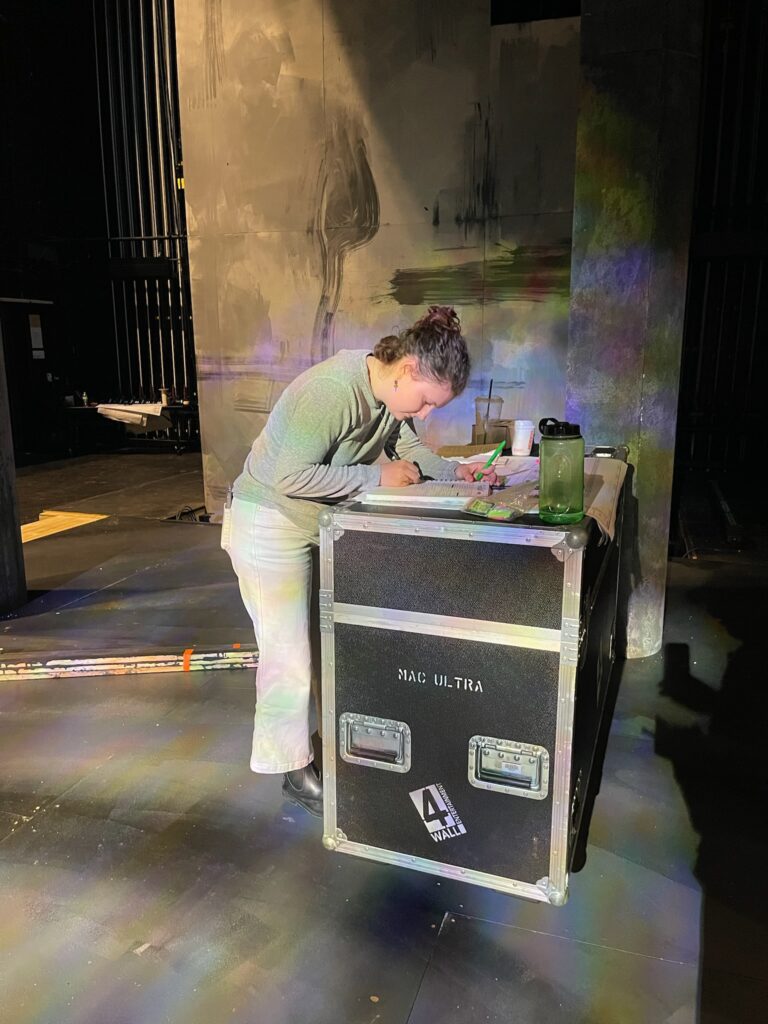 Em Stripling taking notes on a flight case during tech for Fiddler on the Roof, 2023.