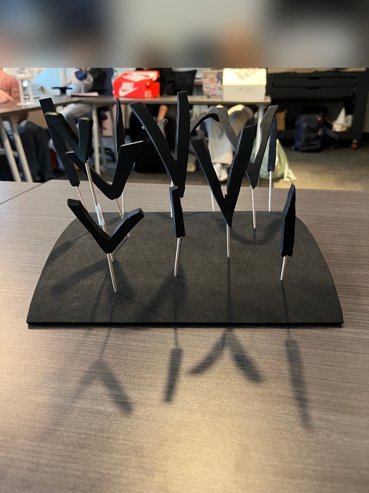 Jacob Anderson · Form & Texture project: a 10×10 EVA foam base with cut-out V-shapes and I-shaped lines in black, mounted on rods at varying heights and planes, casting linear shadows on the surface
