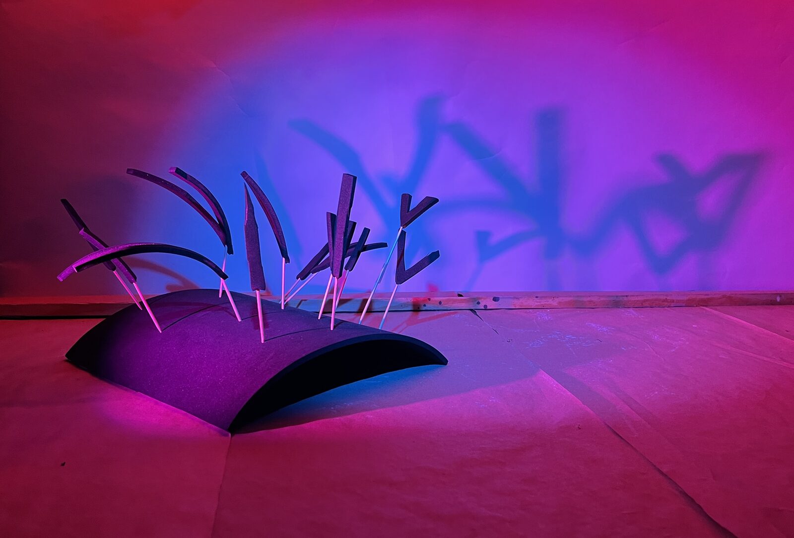 Jacob Anderson · Painting with Light: the Form & Texture model lit from the front with magenta and from behind with deep blue, throwing tall jagged shadows of the V-shapes onto the rear wall