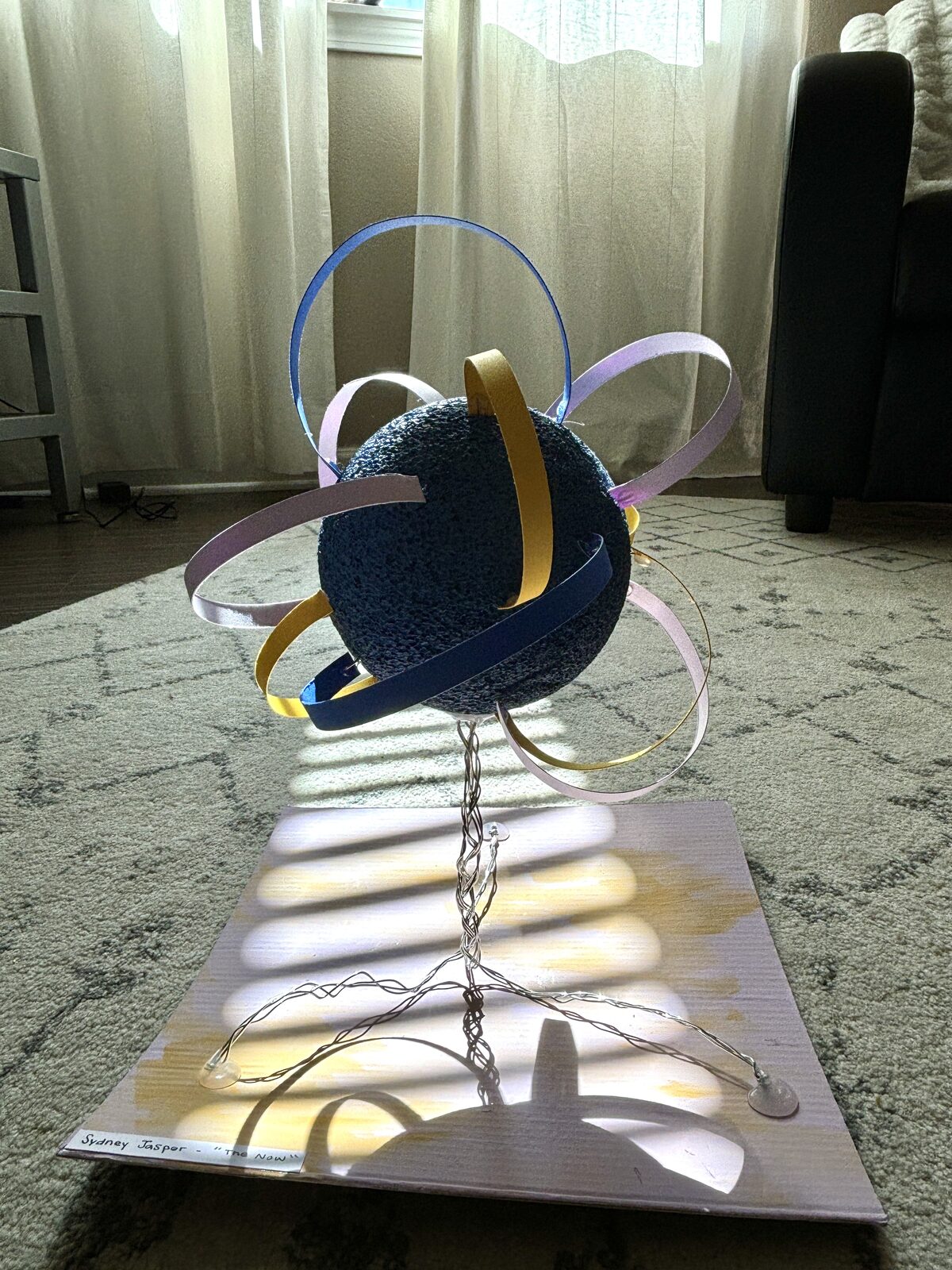 Sydney Jasper · Form & Texture project: a textured indigo foam sphere wrapped in yellow, lavender, blue, and white ribbons, mounted above a square base with a tangled wire-and-cardboard sub-structure